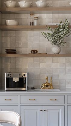 a kitchen with white cabinets and shelves filled with dishes on top of each shelf, next to a gold faucet