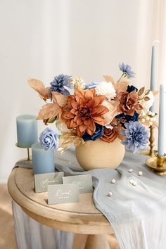 an arrangement of flowers in a vase on a table next to candles and cards with names