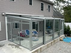 an enclosed patio with two chairs and a table in front of a gray house that is next to a gravel driveway