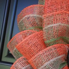 an orange and green mesh wreath is hanging on the front door with a black cat sitting next to it