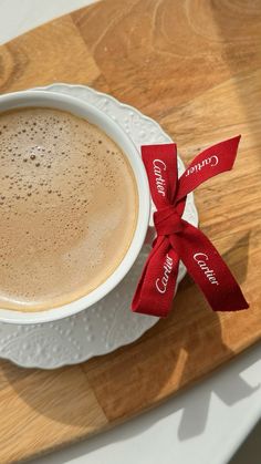 a cappuccino with a red ribbon on a white plate sitting on a wooden table