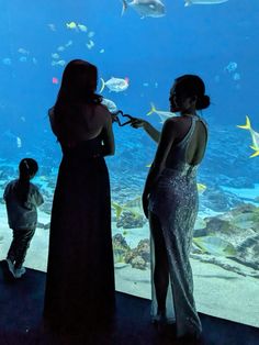 two women standing in front of an aquarium window looking at fish and other marine life