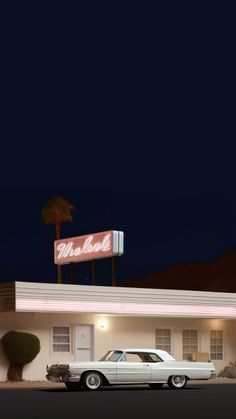 an old white car parked in front of a motel at night with the neon sign above it