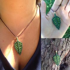 a woman wearing a green leaf necklace next to a tree with her hand in the air