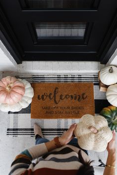 a woman standing in front of a welcome mat with pumpkins and squash on it