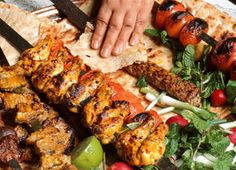 a person is cutting meat on a skewer next to a salad and pita bread