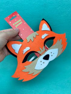 a hand holding a paper mask with an orange fox design on it's face