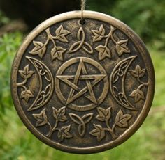 a metal ornament hanging from a string with leaves and an inverted pentagram