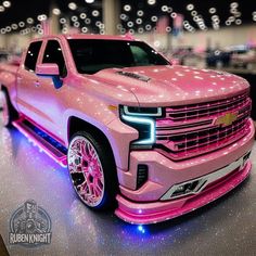 a pink truck is parked in a showroom with lights on it's sides