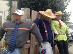 three scarecrows wearing hats and ties standing in front of a fence