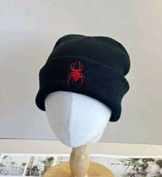 a black beanie with a red spider embroidered on the front and side, sitting on top of a white mannequin head