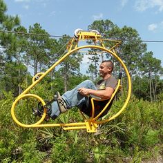 a man sitting on a yellow chair in the middle of trees and bushes while zipping through the air