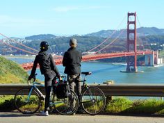 two people standing next to their bikes looking at the golden gate bridge