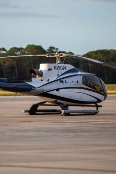 a helicopter sitting on top of an airport tarmac with trees in the back ground