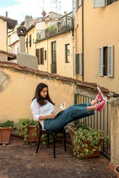 a woman sitting on a chair reading a book in an alleyway with potted plants