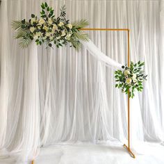 a wedding arch decorated with flowers and greenery for an outdoor ceremony in front of white drapes