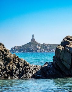 an island with a light house in the distance and blue water around it on a sunny day