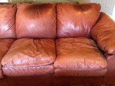 a brown leather couch sitting on top of a carpeted floor next to a window