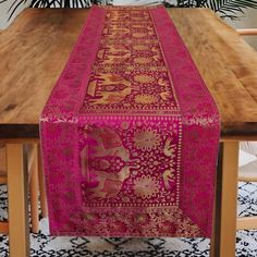 a table with a pink and gold runner on it's side, next to a plant