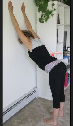 a woman standing on one leg with her hands in the air while leaning against a wall