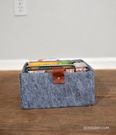 a felt box with several books in it sitting on a wooden floor next to a white wall