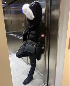 a person standing in an elevator with a handbag on their shoulder and wearing a black jacket