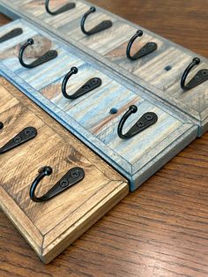 two pieces of metal and wood with hooks on them sitting on a wooden table next to each other