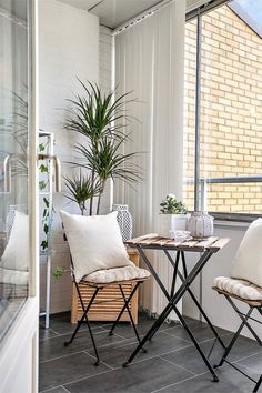 two chairs and a table on a balcony with plants in the window sill next to them