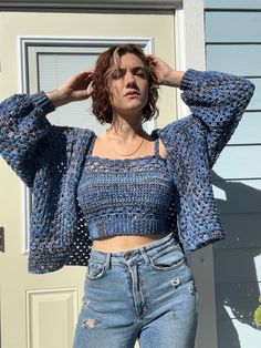 a woman standing in front of a door with her hands on her head and wearing ripped jeans