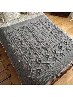 a gray crocheted blanket sitting on top of a wooden floor next to a bed