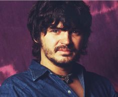 a man with long hair and beard wearing a blue shirt is looking at the camera