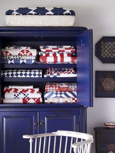 a blue china cabinet with red, white and blue quilts on it's shelves