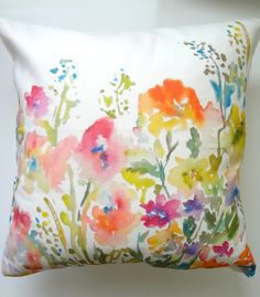 a white pillow with colorful flowers on the front and back side, sitting against a wall