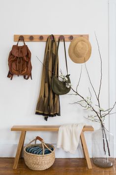 a wooden bench sitting under a coat rack with hats and scarves hanging on it