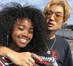 two young people standing next to each other in front of a parking lot with cars