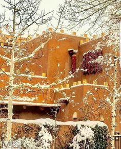 an adobe style building with snow on the ground and trees in front of it,