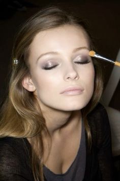 a woman with makeup brush in her mouth and eye shadow on her face, looking at the camera