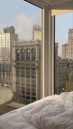 a bed in front of a large window with city buildings out the window behind it