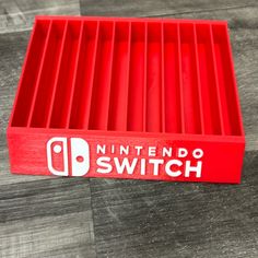 the nintendo switch logo is displayed on a red plastic box that sits on a wood floor