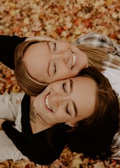 two women are laying on the ground covered in leaves and looking up at the camera