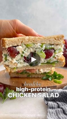 a person is holding a sandwich with chicken salad on it and grapes in the background