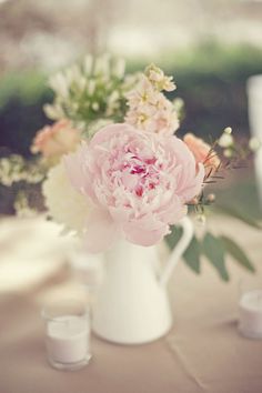 a white vase filled with pink flowers on top of a table