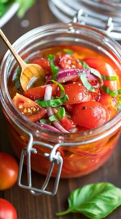 a glass jar filled with tomato salad on top of a wooden table next to tomatoes and basil