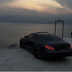 a black car parked on the beach at sunset