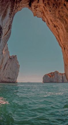 an arch in the side of a large body of water with rocks sticking out of it