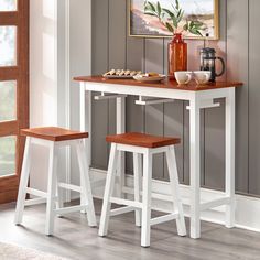 two stools and a table with food on it in front of a painting hanging on the wall