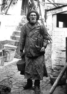 an old photo of a man standing in front of a building with buckets on his shoulder