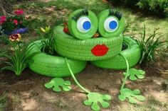 a green frog statue sitting on top of a lush green grass covered field next to flowers