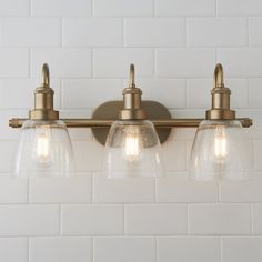 three clear glass shades are on the brass bathroom light fixture