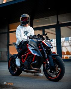 a man sitting on top of a motorcycle in front of a building and wearing a helmet